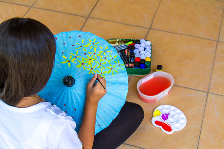 Asia girl paint yellow flower on blue umbrella with paintbrush.の写真素材