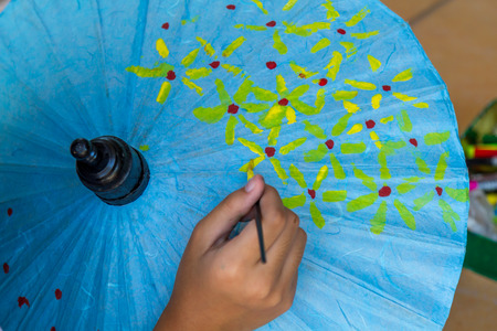 Asia girl paint yellow flower on blue umbrella with paintbrush.の写真素材