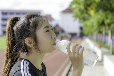 Asia girl hold a bottle of water after exhaustion exercise background outdoor stadium.の写真素材