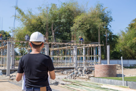 Engineers wear a helmet and holding construction plan monitoring the construction area.