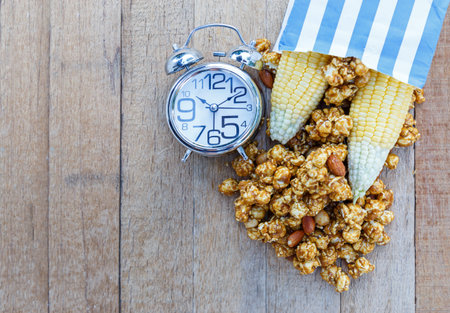 Popcorn caramel mix macadamia and almond taste in paper bag and alarm clock on wood table with copy...