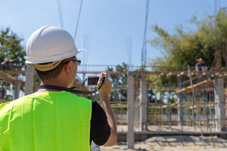 Engineers wear a helmet and holding construction plan and camera monitoring the construction area.の写真素材