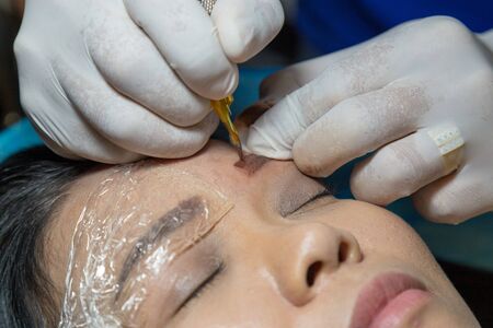 Asia woman tattoo eyebrow by using the electric tattoo machine by beautician professional in beauty salon.の写真素材