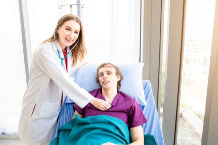 The female doctor is wearing a doctor uniform use the stethoscope to check the pulse of the male patient lying on the bed. Concept examination of the symptoms of diseases such as colds.の写真素材