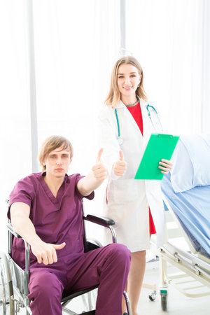 The male patient wearing in a patient dress in a wheelchair seemed happy to recover from illness or to go home in a hospital or clinic room.の写真素材