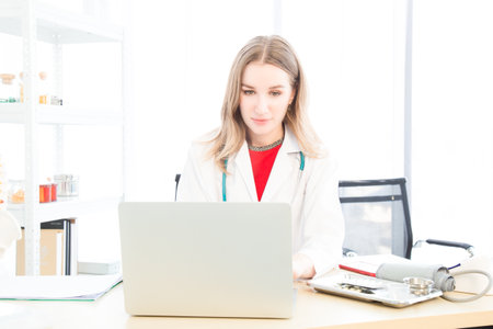 A female beautiful doctor is wearing a doctor uniform have a stethoscope using a notebook computer or laptop and talking case of treatment in the examination room in the hospital or clinic.の写真素材