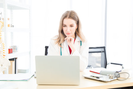 A female beautiful doctor is wearing a doctor uniform have a stethoscope using a notebook computer or laptop and talking case of treatment in the examination room in the hospital or clinic.の写真素材