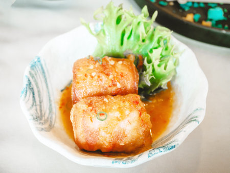 Fried bacon wrapped snapper fish spicy sauce in a ceramic bowl on table in the restaurant.の写真素材