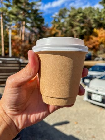 A person is holding a cup with a lid on it. The cup is brown and has a white lidの写真素材