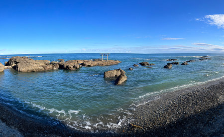 Torii of Ooarai Isosaki Shrine, A rocky shoreline with a small shrine on top of a rock. The water is calm and the sky is clearの写真素材