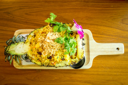 Pineapple baked rice in pineapple fruit on wood plate at restaurant. top view.の写真素材
