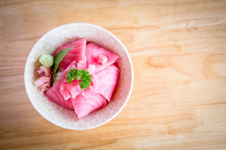 Japan food Tuna or Maguro don Consisting of sliced Tuna or Maguro on top of Japanese rice Served with wasabi and pickled ginger in a white bowl on a wooden table.の写真素材