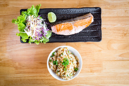 Salted Grilled Salmon served with salad and garlic fried rice on a black ceramic plate on a wooden table with copy space.の写真素材