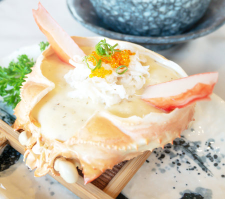Snow crab baked with mushroom cream sauce on the crab shell with topping made of orange roe placed on a wooden sieve on a white ceramic plate in the restaurant.の写真素材