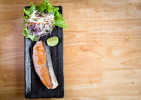 Salted Grilled Salmon served with lemon and salad on a black ceramic plate on a wooden table with copy space.の写真素材