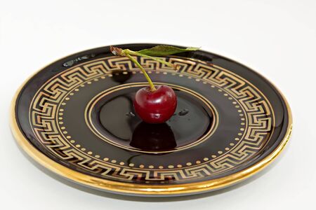 One cherry on the black with gilding saucer. White background. Isolatedの写真素材