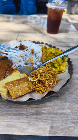 close up food of pecel rice with fried noodles, tempeh, tofu and omelette on the beachの写真素材