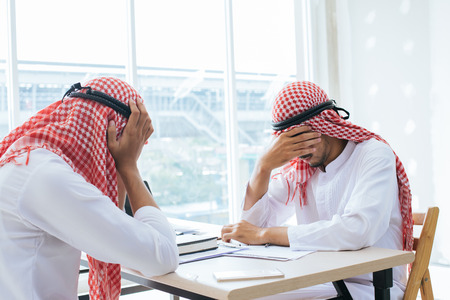 Two Arab businessmen sitting inside the office building are  having headache to work at the meeting.の写真素材