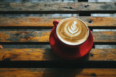 Close up a cup of hot coffee or cappuccino is placed on an outdoor wooden table in the morning. Warm festival with warm drinks in the winter.の写真素材