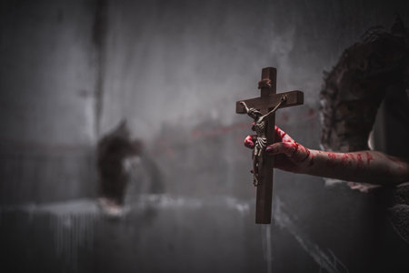Close up bloody hands holding the crucifix of Jesus on a black background, Symbol of belief and...