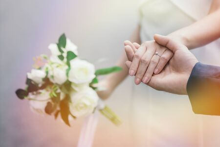 Close-up image of the groom holding the bride's hand with the ring on the hand. Romantic young couples enjoy the morning sun on the wedding day.の写真素材