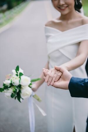 Close-up image of the groom holding the bride's hand with the ring on the hand. Romantic young couples enjoy the morning sun on the wedding day.の写真素材