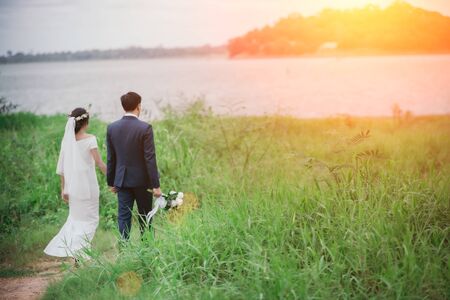 Couples in romantic wedding dresses are enjoying a stroll through the beautiful sunset with a green grass background. Warm love on valentine's day.の写真素材