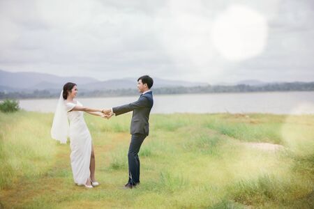 Marriage or valentines day concept - The groom and the bride dressed in white are dancing on the green fields on his wedding day. Young lovers are walking hand in hand in the garden.の写真素材
