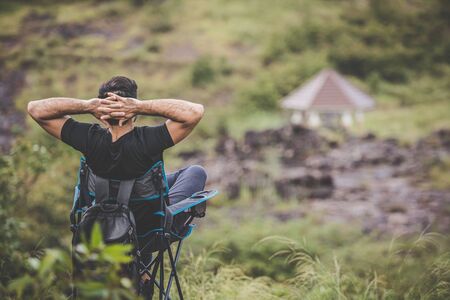 Camping in the middle of nature mountains with fresh air. Young man sat in a relaxing chair on his vacation. の写真素材