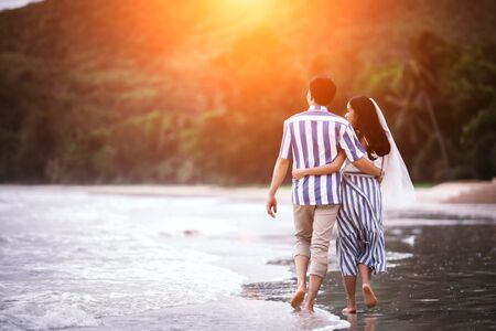 Couples young man and women are embracing each other to see the sea and sunset along the coastline. Romantic couple relaxing on the beach.の写真素材