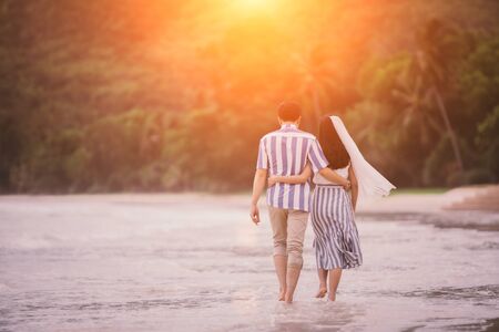 Couples young man and women are embracing each other to see the sea and sunset along the coastline. Romantic couple relaxing on the beach.の写真素材