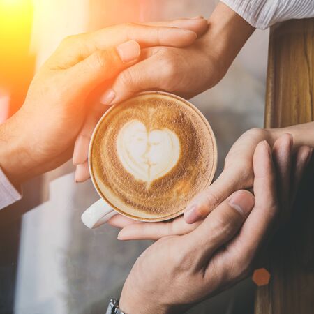 Valentine day, Top view of a young lovers hand holding a heart shaped coffee cup on a wooden table in the coffee shop. Warm Tone.の写真素材
