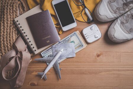 Travel concept - Top view model plane with passport, Yellow hat and smartphone and headphones and bag on a wooden table. Traveler accessories.の写真素材