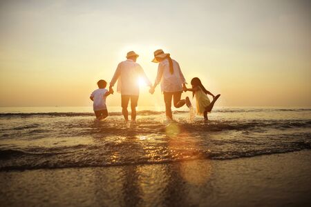 Summer vacations. Happy family is holding hands running on the beach at sunset. Father and mother and little children are having fun on a tropical beach.の写真素材
