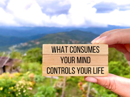 Hand holding wooden block with words What Consumes Your Mind Controls Your Life with blurred backgroundの写真素材