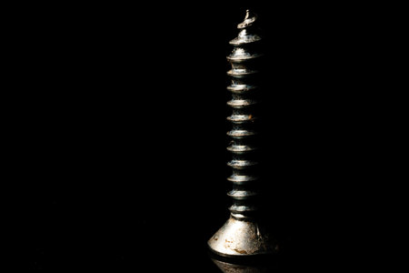 An isolated screw placed on a reflective surface with a dark background