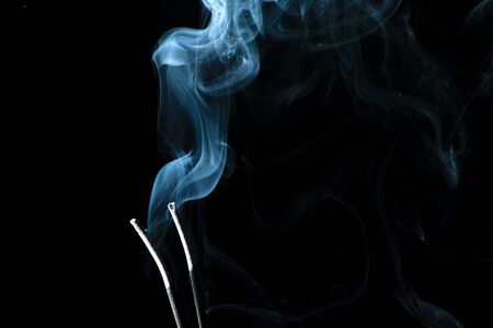 White puffed smoke coming out of sticks in a dark backgroundの写真素材