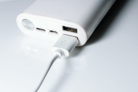 A white power bank with USB ports and power button. A cable is attached to one of its ports