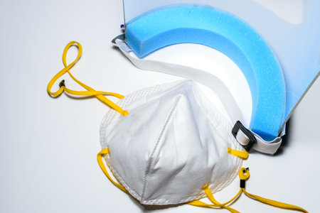 A face mask and a face shield placed on a white surface. To use for personal protection against...