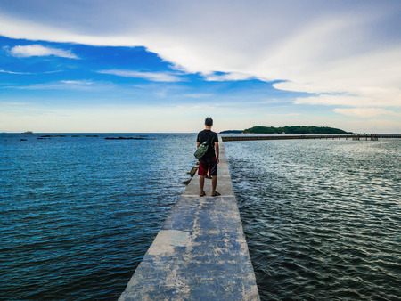 Asian guy stand on Concrete bridges on the ocean with idyllic ocean and beautiful Sky in vacation time,Holiday in the sea,Summer conceptの写真素材