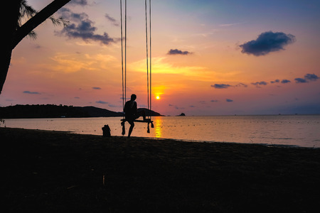 Silhouette People sit on the swing with beautiful sunset cloud sky on the idyllic ocean in vacation time,koh mak island thailand,summer conceptの写真素材