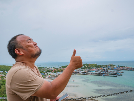 Asisn Fat Traveler make a thumb up pose on top of  Khao Ma Jor Pier  with Idyllic ocean beautiful white cloud and Fishman townscape in vacation time,chonburi thailand,holiday conceptの写真素材
