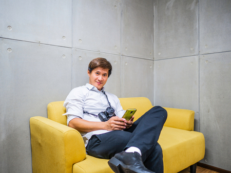 Handsome Asian man Sitting on yellow sofa while play mobliephone,Relax conceptの写真素材