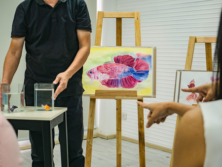 senior adult artist teacher teaching his student in the class room,fish and art drawing conceptの写真素材