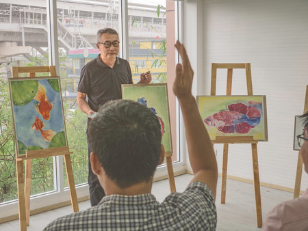 senior adult artist teacher teaching his student put hand up and ask question in the class room,fish and art drawing conceptの写真素材