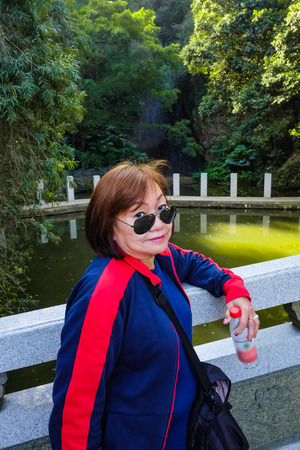 Senior women tourist stand beside the Lake on top of the xiqiao mountain foshan city chinaの写真素材