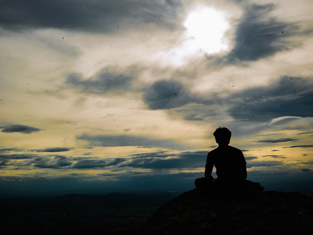 Silhouette Photo of Tourist sitting on the Rocky cliff on Khao Luang mountain in Ramkhamhaeng National Park,Sukhothai province Thailandの写真素材