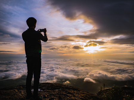 Silhouette People Take a Picture on the cliff with beautiful sunrise sky on Khao Luang mountain in Ramkhamhaeng National Park,Sukhothai province Thailandの写真素材