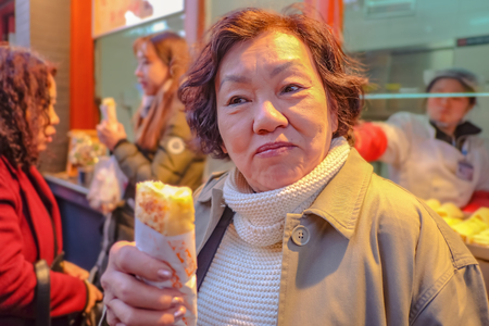 Portrait Photo of Senior asian women Holding Spring roll in Wangfujing Walking street and street food in beijing city, China travelのeditorial素材