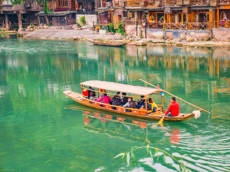 fenghuang,Hunan/China-16 October 2018:Unacquainted tourist sightseeing fenghuang old town architecture by boat in the river.phoenix ancient town or Fenghuang County is a county of Hunan Province, Chinaのeditorial素材